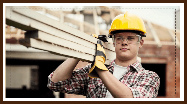 A man in hard hat and gloves carrying wood.